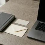 Zamknięty notes, neutralna karta i dokumenty ułożone przy laptopie na biurku